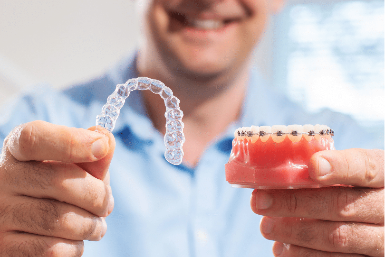 Man holding an Invisalign Clear Aligner next to a model of traditional braces