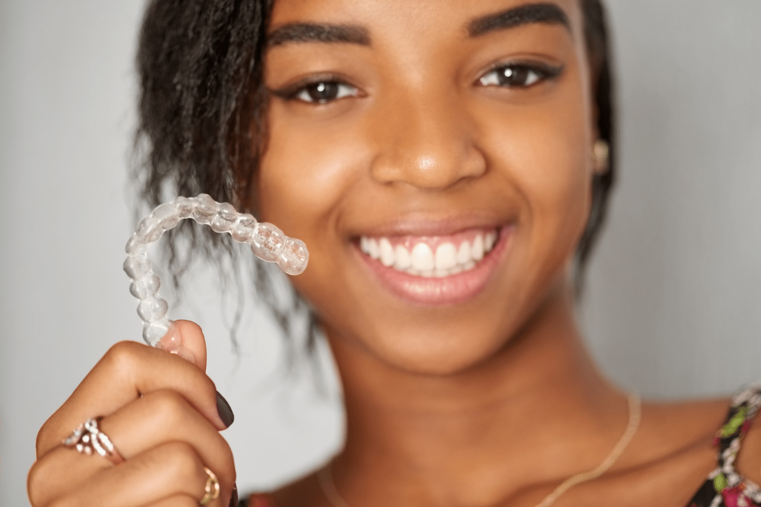 Woman smiling holding Invisalign Clear Aligner