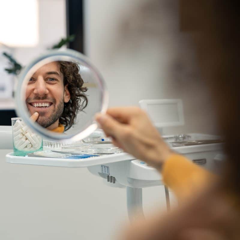 man looking into a mirror smiling, pointing to his new implant tooth