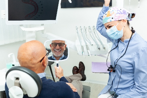 man smiling in mirror, happy with new dental implant