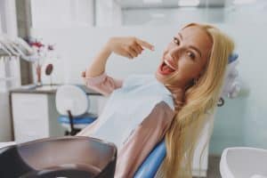 blonde haired woman sitting in a dental chair, pointing to her new smile