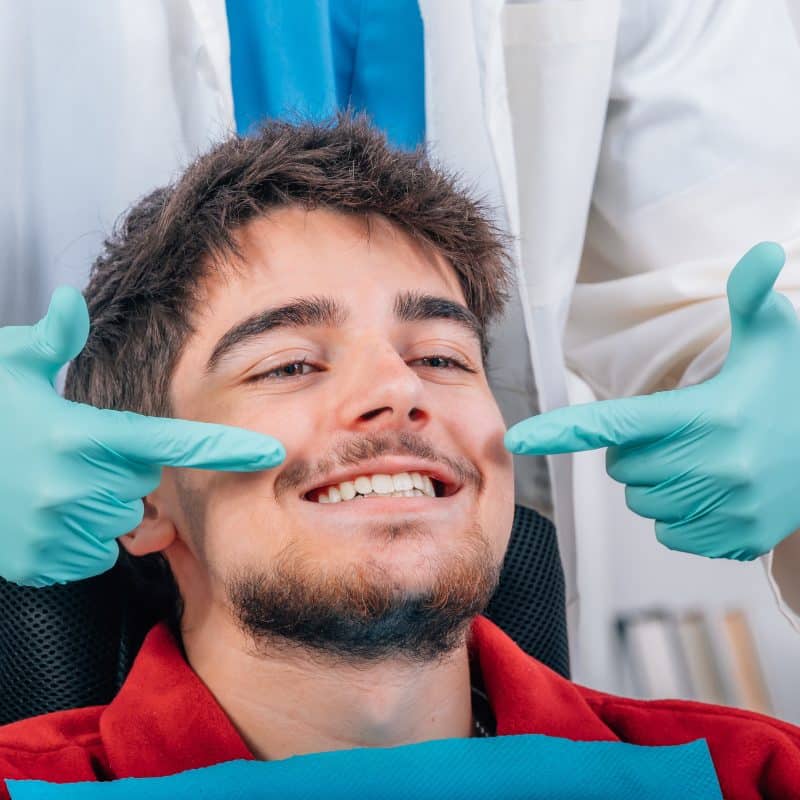 dentist in blue gloves showing with hands the mouth and smile of the patient