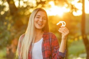 Woman holding invisalign braces outdoors, sunset