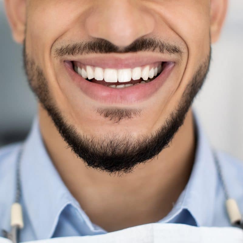 Dental treatment result. Close-up shot of a happy young man smiling broadly with his perfect white teeth while sitting in the dentist's chair